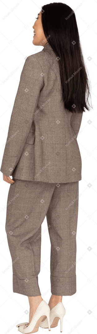 Three-quarter back view of a smiling young lady in brown business suit