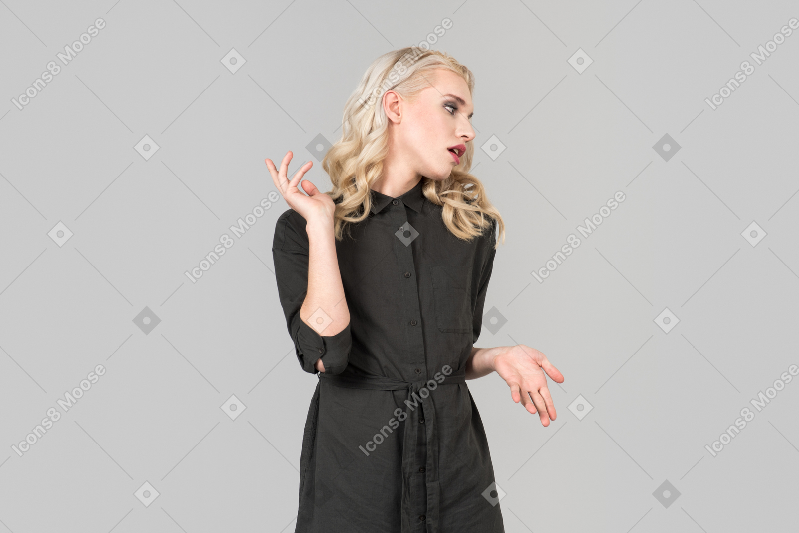 Uma jovem de cabelos loiros em um vestido preto de pé contra o fundo cinza liso