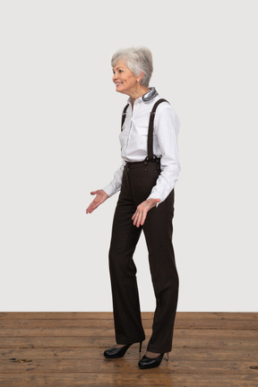 Трехчетвертный вид улыбающейся жестикулирующей старушки в офисной одежде