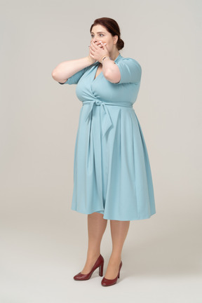 Vista lateral de uma mulher assustada com um vestido azul cobrindo a boca com as mãos