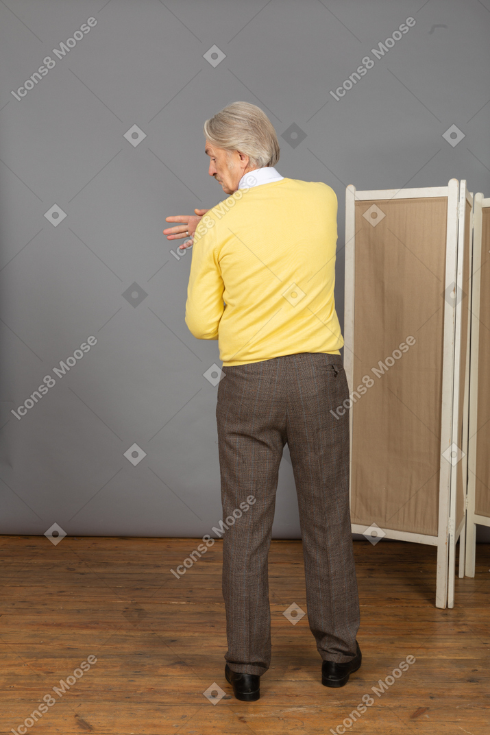 Back view of a gesticulating old man looking aside while touching shoulder