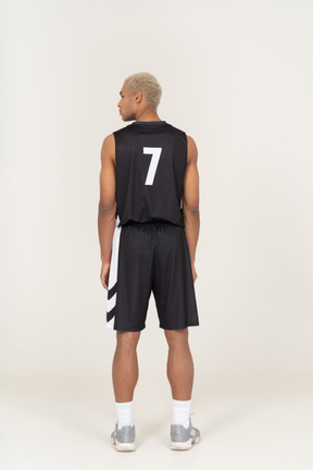 一个年轻的男篮球运动员站着不动，看着一旁的背影