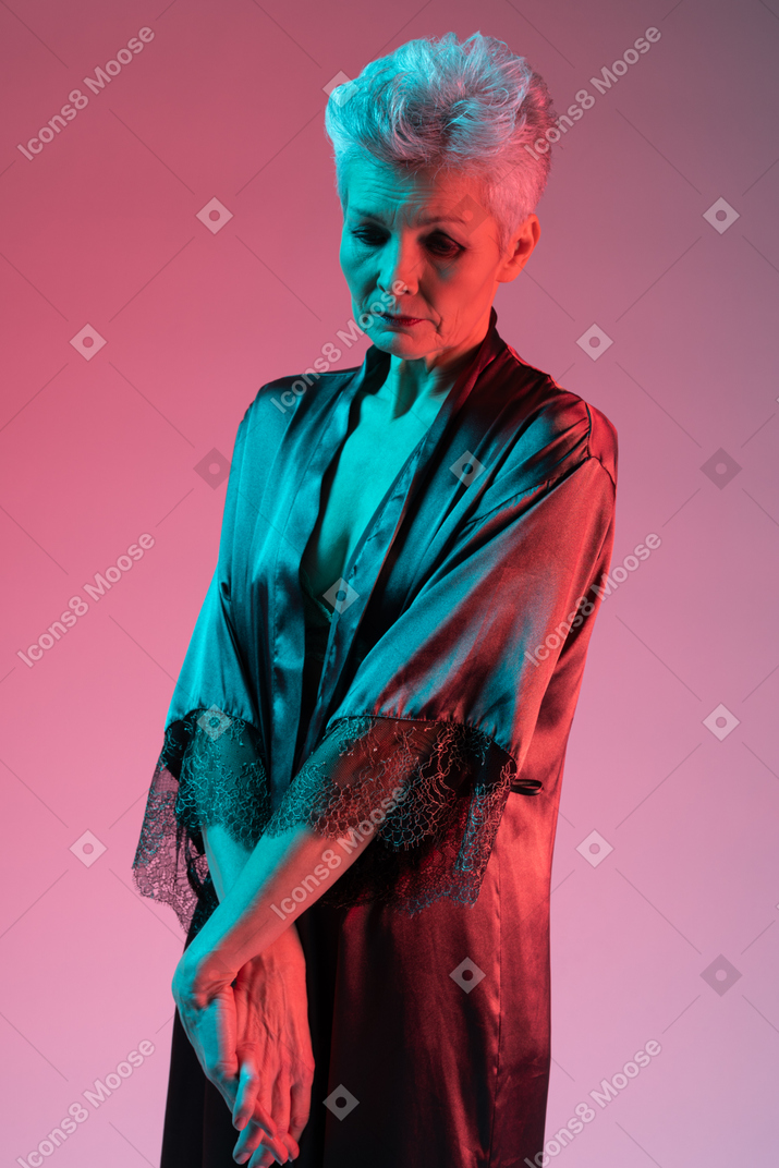 Sad elderly lady standing with crossed hands and looking down