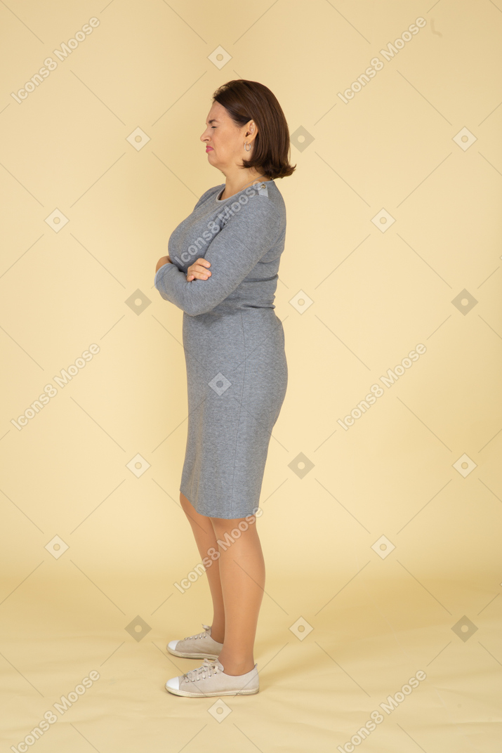 Вид сбоку на женщину в сером платье, стоящую со скрещенными руками