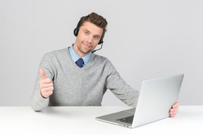 Agente de call center, sentado na mesa do escritório e mostrando o polegar para cima