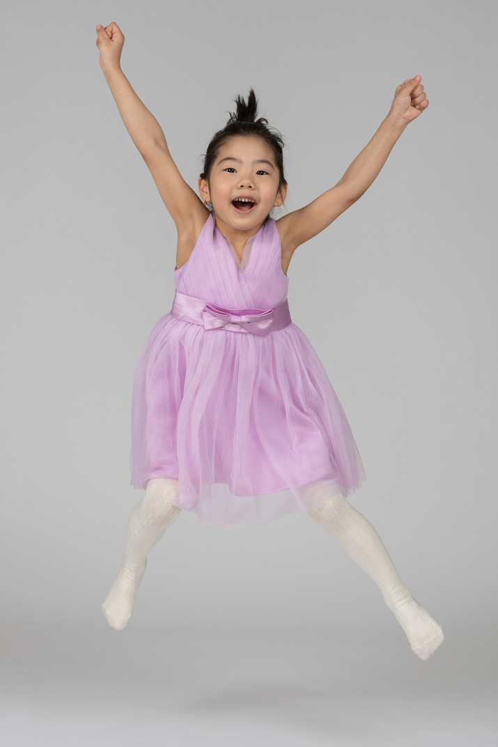 Happy girl in a pink dress jumping with her arms and legs spread