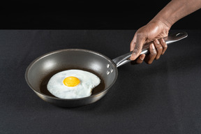 Human arm holding a fried egg on pan