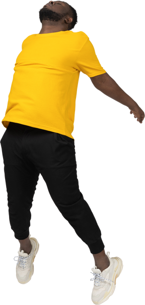 Three-quarter view of a jumping young dark-skinned man in yellow t-shirt outspreading hands