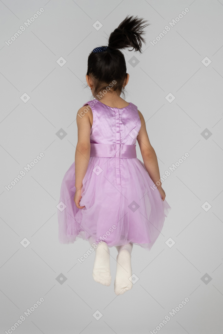 Back view of a girl in pink dress jump with folded legs