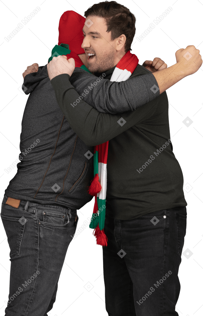 Вид сбоку двух эмоционально обнимающихся футбольных фанатов мужского пола, сжимающих кулаки