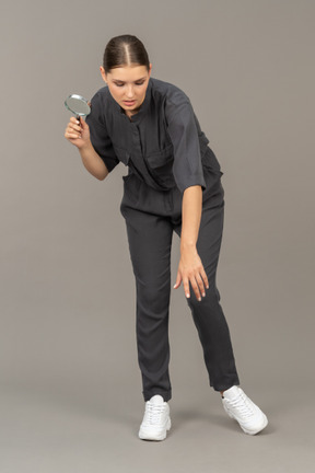 Front view of a young woman in a jumpsuit holding a magnifying glass