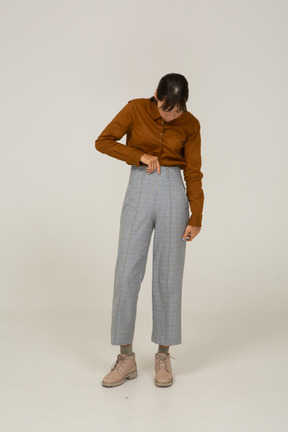 Vista frontale di una giovane donna asiatica in calzoni e camicetta che tocca i pantaloni e guarda in basso