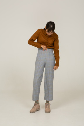 Front view of a young asian female in breeches and blouse touching trousers and looking down