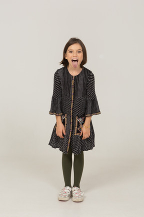 Vista frontale di una bambina vestita che si sporge in avanti e mostra la lingua