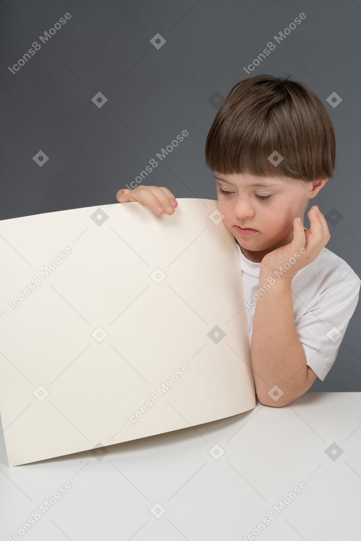 Serious little boy holding a sheet of paper