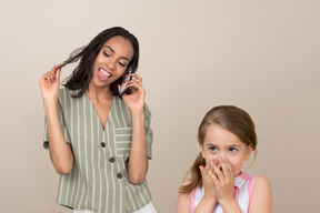 Mulher atraente, falando ao telefone e menina envergonhada com o que ela ouve