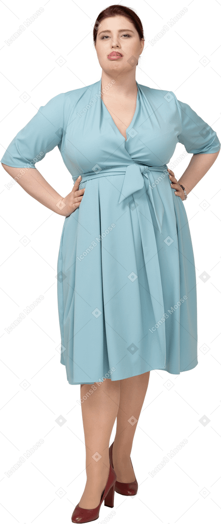 Vue de face d'une femme en robe bleue debout avec les mains sur les hanches et faisant des grimaces