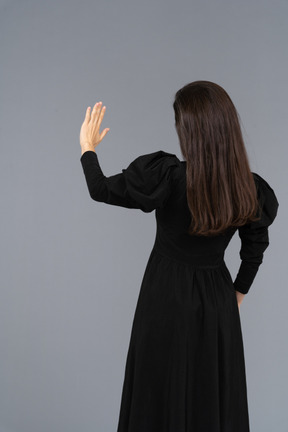 Rückansicht einer jungen dame in einem schwarzen kleid, die ihre hand hebt