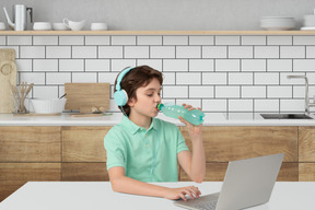 Boy drinking water from a bottle while using a laptop