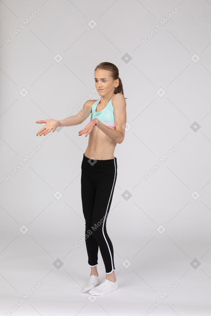 Vista de tres cuartos de una jovencita disgustada en ropa deportiva extendiendo las manos