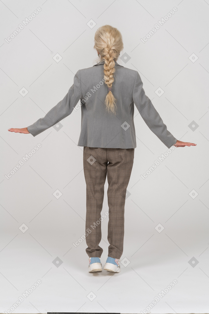 Vista posterior de una anciana en traje de pie sobre los dedos de los pies y los brazos extendidos