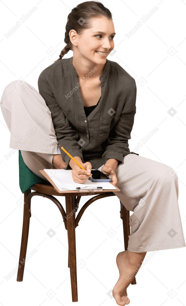 Vista frontal de uma jovem sorridente, vestindo roupas de casa, sentada em uma cadeira e fazendo anotações