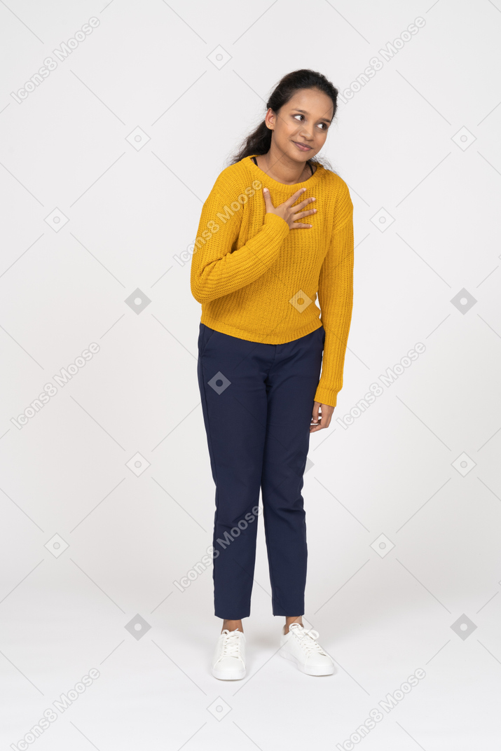 Vista frontal de una niña feliz en ropa casual posando con la mano en el pecho