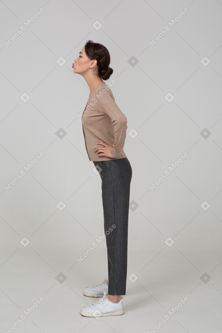 Side view of a young lady in pullover and pants sending an air kiss and putting hands on hips