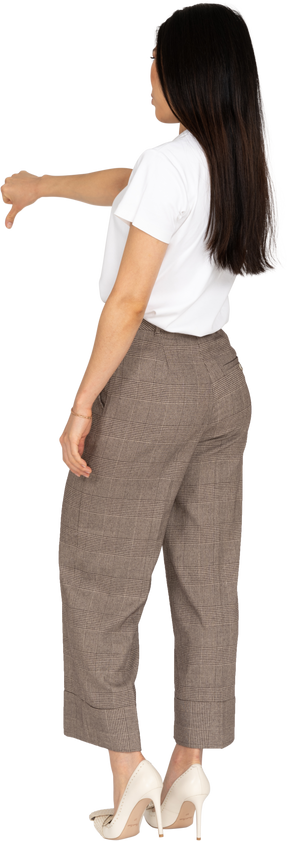 Vista posteriore di tre quarti di una giovane donna in calzoni e maglietta che mostra il pollice verso il basso