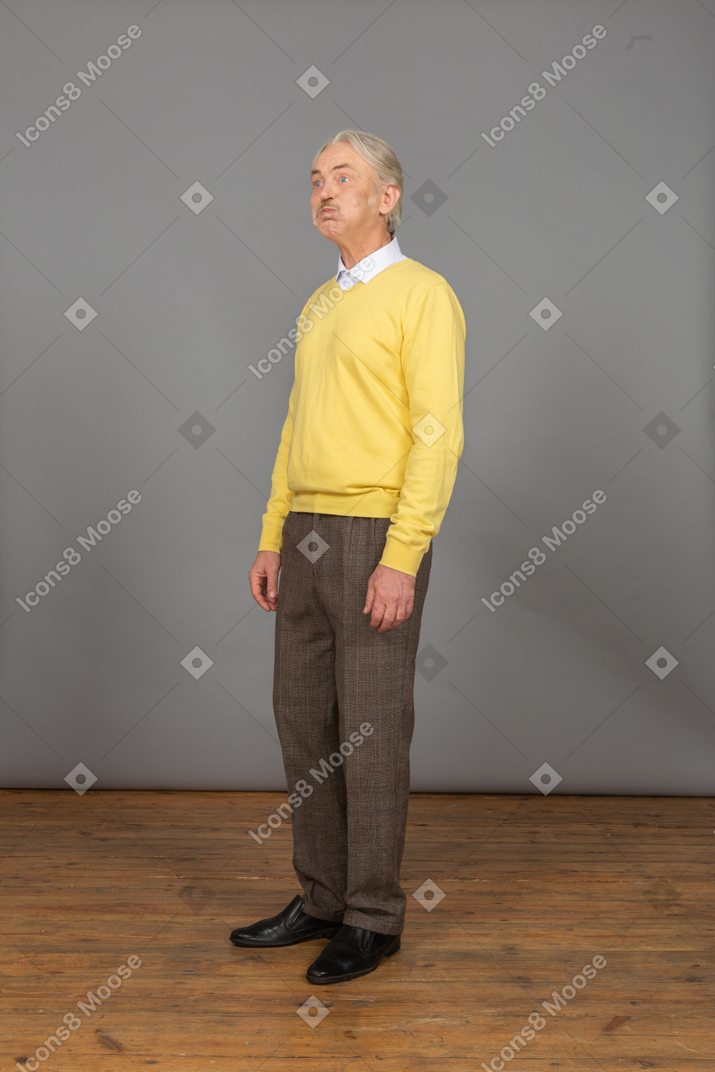 Vista de três quartos de um homem velho fazendo beicinho em um pulôver amarelo olhando para o lado e fazendo careta
