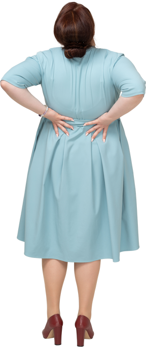 Вид сзади женщины в синем платье, страдающей от боли в пояснице