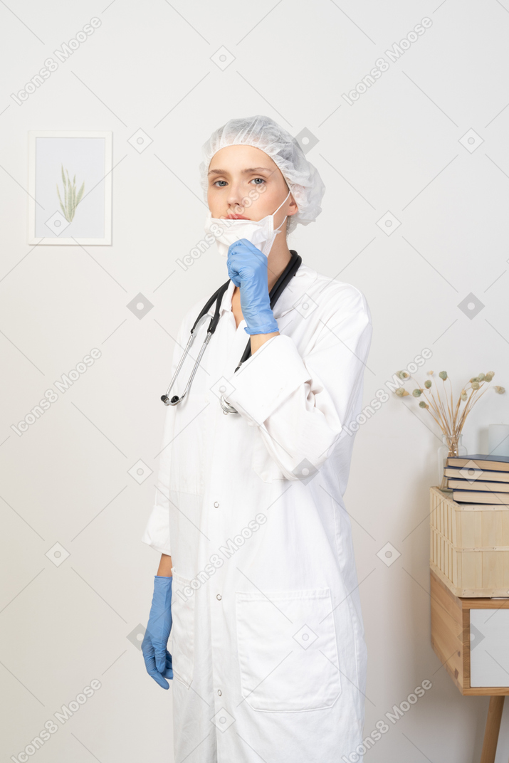Vista de três quartos de uma jovem médica colocando uma máscara e olhando para a câmera