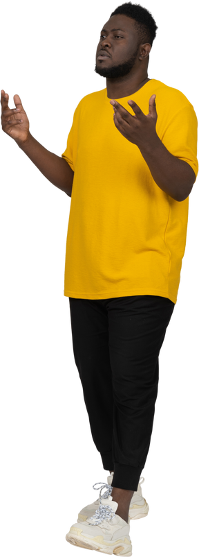 黄色のtシャツを着た思慮深い身振りで示す若い浅黒い肌の男の4分の3のビュー