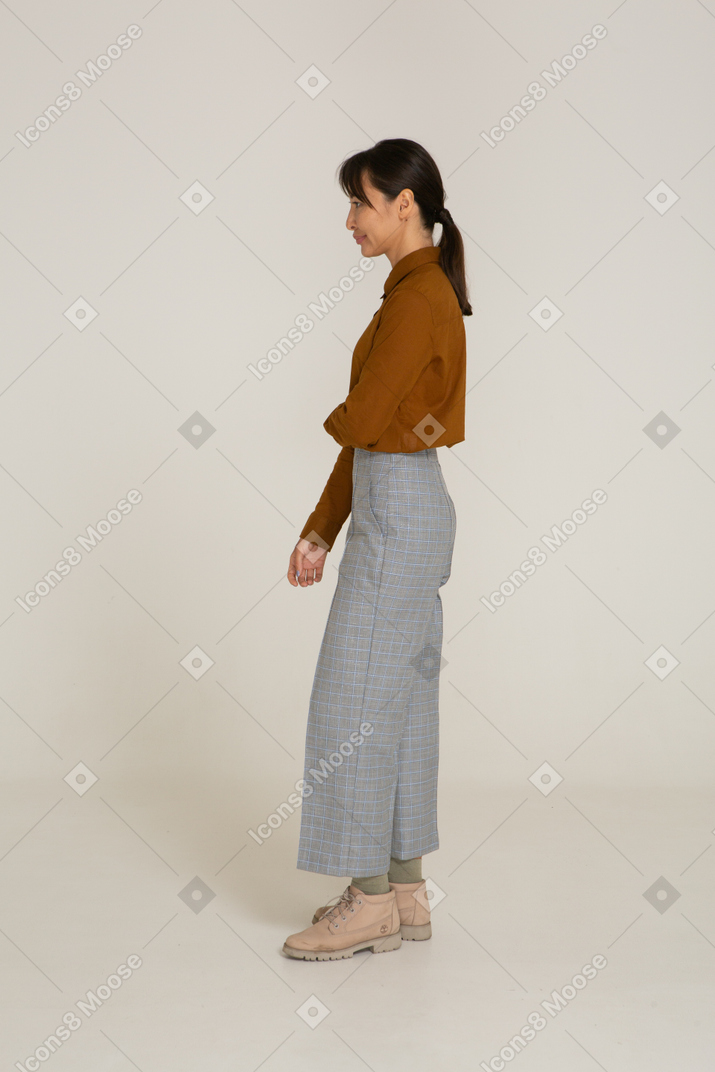 Vista lateral de uma jovem mulher asiática fazendo beicinho de calça e blusa segurando o braço dela