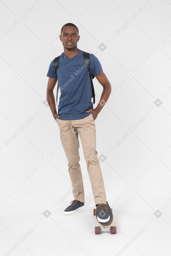 Black male tourist standing with one leg on skateboard and holding his hands in the pockets