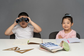 Smiling little girl and boy looking through binoculars