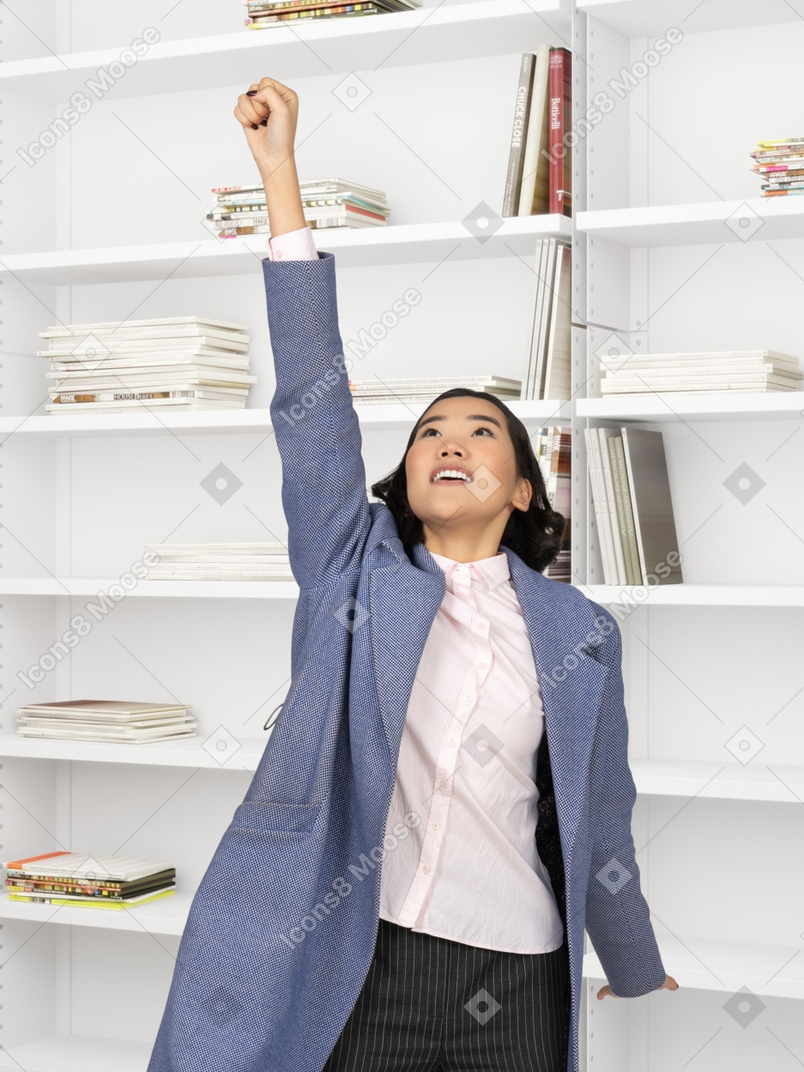A woman standing in front of a bookshelf and raising up her arm