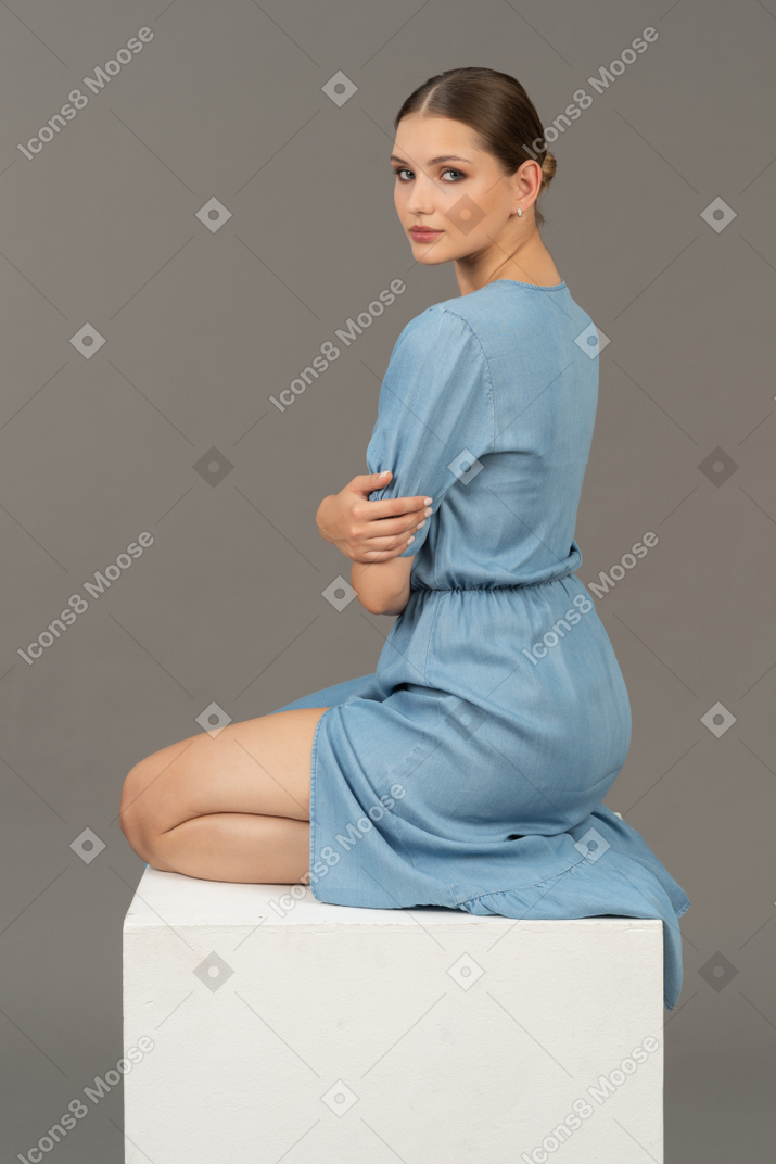 Vista traseira do jovem de vestido azul, sentado no cubo