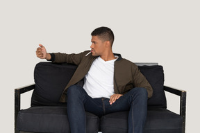 Front view of young man sitting on a sofa and holding cigarette in mouth