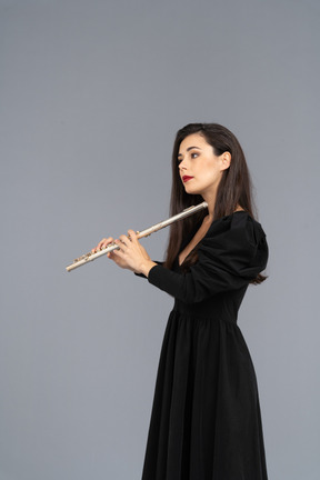 Side view of a serious young lady in black dress holding flute