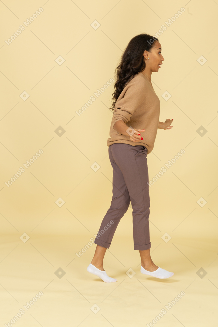 Side view of a dark-skinned walking young female outspreading her hands