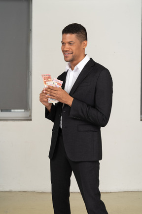 Three-quarter view of a young man in black suit holding banknotes