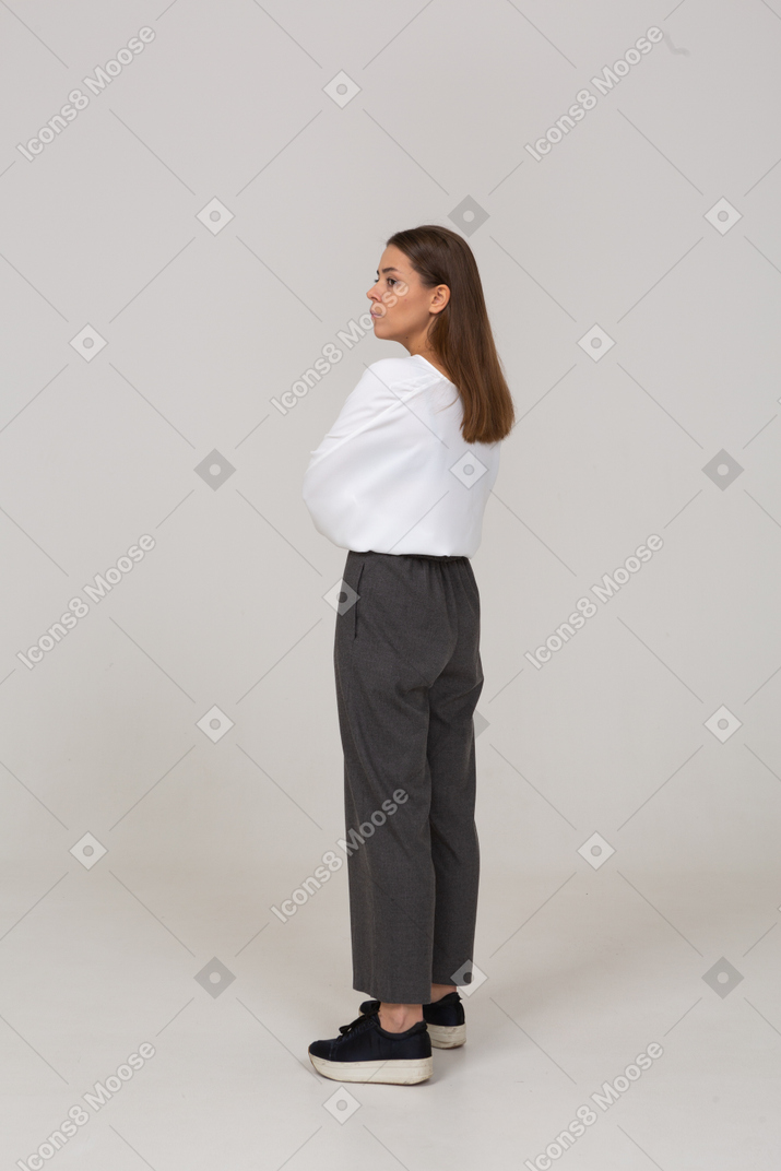 Vista traseira de três quartos de uma jovem preocupada em roupas de escritório, cruzando os braços