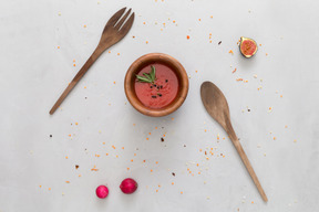 A bowl of tomato sauce, wooden fork and spoon, some radish and a fig