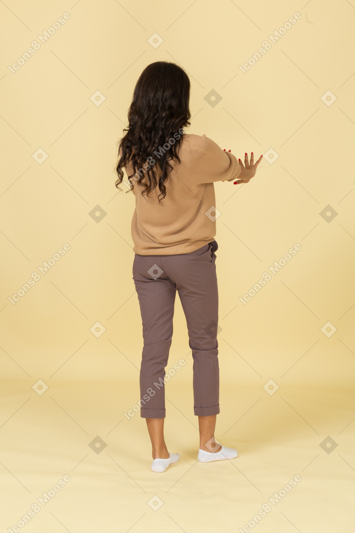 Vista traseira a três quartos de uma jovem mulher de pele escura estendendo as mãos