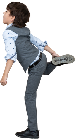 Vista lateral de um menino de terno cinza em pé em uma perna