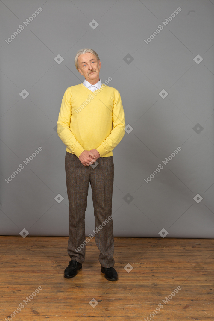 一个困惑的老人，手牵着手，穿着黄色套头衫的前视图