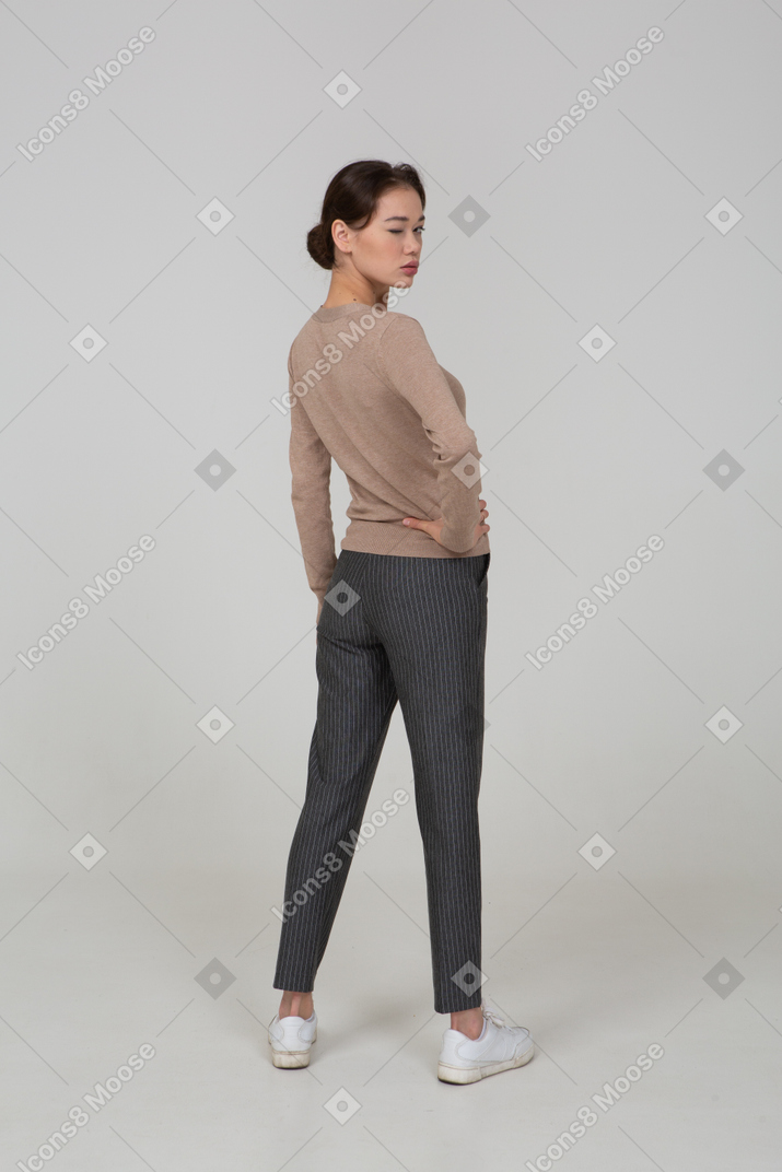 四分之一的后视图的眨眼的年轻女士穿着套头衫和裤子放在臀部上的裤子