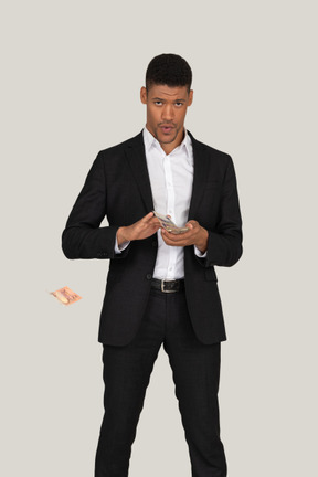 Front view of a young man in black suit wasting money