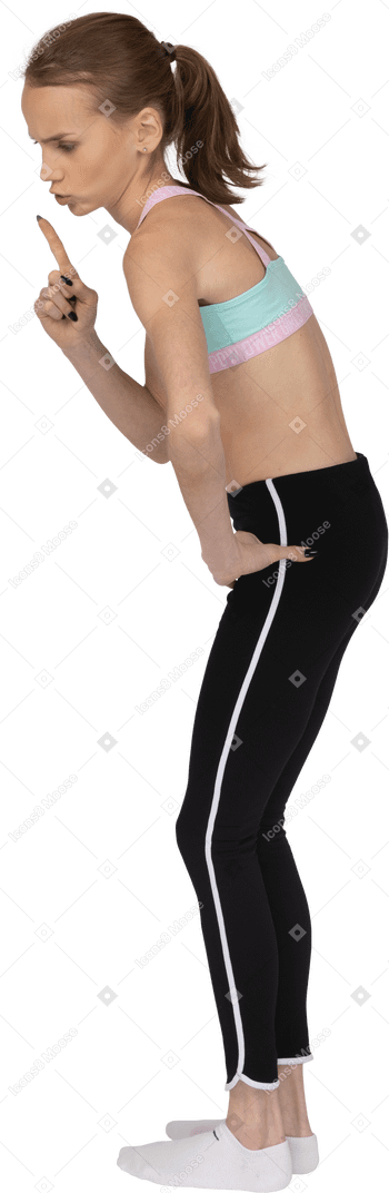 Vista lateral de uma adolescente em roupas esportivas mostrando um gesto de silêncio